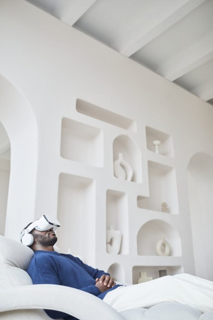 pexels-photo-7432039 Man sitting on a sofa using a virtual reality headset in a modern, minimalist indoor setting.